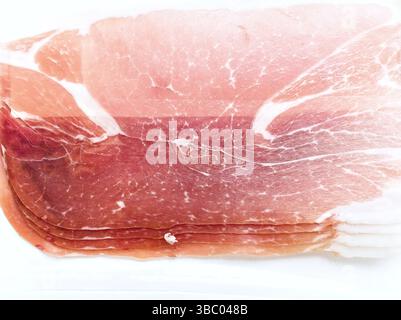 Ein Stück Fleisch mit rosafarbener Farbe. Sie wird in Scheiben geschnitten und auf eine weiße Platte gelegt Stockfoto