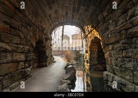 Central Park an einem kühlen Februartag, vorbei an verwitterten Steinbögen. Die Sonne strahlt ein warmes Licht über das ruhige Wasser Stockfoto