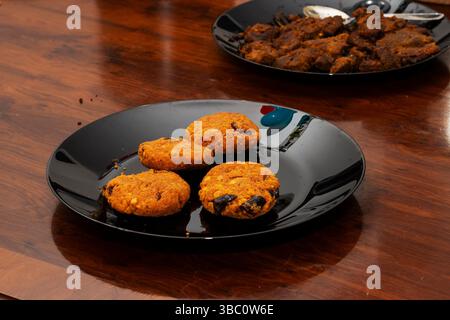 Blick aus der Nähe auf das traditionelle südindische Parippu Vada oder Dal Fritters serviert auf einem schwarzen Teller über einem Holztisch Stockfoto