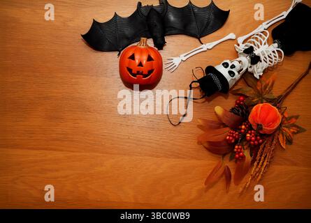 Eine festliche Halloween-Wohnung mit einer Jack-o'-Laterne, schwarzer Fledermaus, Skelett mit Kopfhut und Herbstdekorationen mit Beeren und Blättern Stockfoto