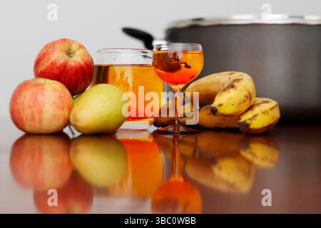 Eine lebendige Stillleben-Komposition mit frischen Äpfeln, Bananen und Birnen sowie Gläsern bernsteinfarbenen Safts, die auf einer reflektierenden Küche platziert werden Stockfoto