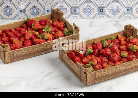 Zwei Kisten frischer Erdbeeren auf einer Marmorplatte, blaues Muster im Hintergrund Stockfoto