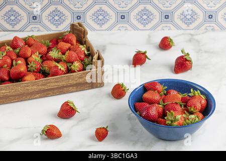 Frische Erdbeeren in einer blauen Schüssel und eine Pappschachtel auf einer Marmorplatte Stockfoto