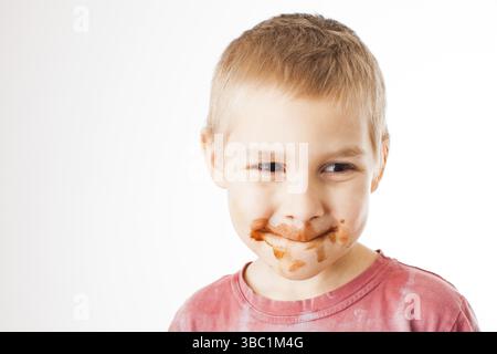 Porträt der blonde Junge mit Schokolade auf seinem Gesicht isoliert auf Weiss. Junge nach Schokolade Eis essen Stockfoto