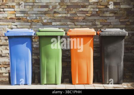 Vier Kunststoff-Abfallbehälter in verschiedenen Farben zur Mülltrennung. Sammeln und Trennen von Müll für die weitere Verarbeitung. Wand mit Deko Stockfoto