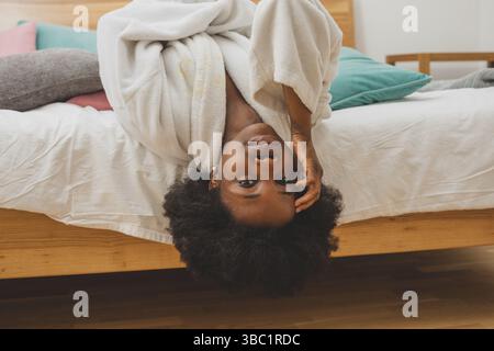 Die glückliche junge Frau im Bademantel liegt auf dem Bett und stellt sich auf den Kopf. Die Frau entspannt sich im Spa Stockfoto