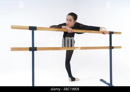 Eine junge Ballerina in schwarzem Trikot zeigt eine Eversion der Füße und dehnt sich beim Aufwärmen an der Barre Stockfoto