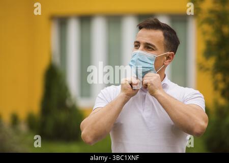 Der gutaussehende junge Mann, der in der Stadt eine medizinische Maske verkleidet. Er trägt ein stilvolles weißes T-Shirt Stockfoto