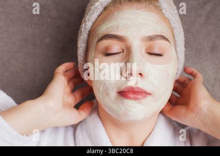 Das schöne Mädchen liegt mit geschlossenen Augen und berührt die Hände ihres Gesichts. Frau mit Tonmaske Stockfoto
