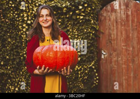 Fröhliche Frau mit großem Kürbis in den Händen auf dem Bauernhof, die fröhlichen Thanksgiving-Tag zu feiern Stockfoto