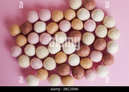 Nahaufnahme von oben Wollkugeln in abstrakter Form auf rosa Oberfläche. Sortiment an handgefertigten Filzperlen in den Farben Pink, weiß, Beige und Gelb Stockfoto