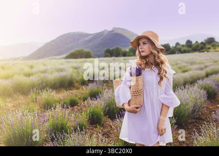 Porträt einer schönen blonden Frau, die zwischen den Plantagen von Lavendel steht. Mädchen in einem weißen Sundress gekleidet und hält sbunch Lavendel Stockfoto