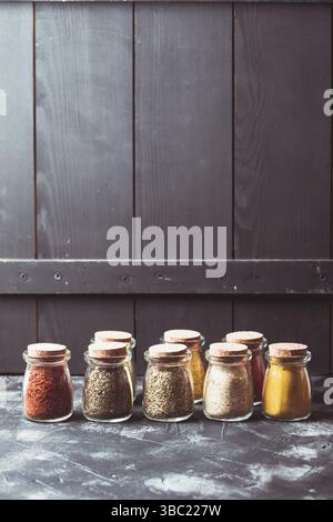 Verschiedene gemahlene Gewürze in alten Glasflaschen über Holzwand, Kopier-Cpase Stockfoto