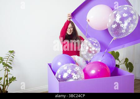 Die glückliche junge Frau öffnet eine große geschenkbox. Die wunderschönen Ballons fliegen aus der Box Stockfoto