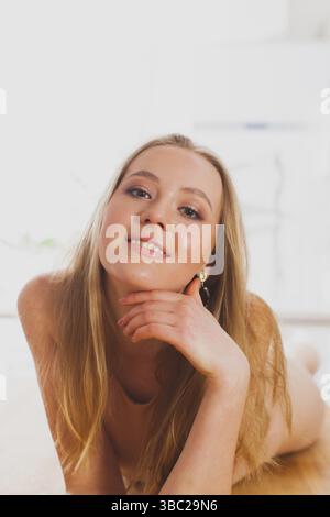 Porträt einer charmanten blonden Frau mit lockerem Haar, die sich auf einem Holzboden posiert. Ein lächelndes Modell, das natürliche Schönheit mit minimalem Make-up zeigt. Whit Stockfoto