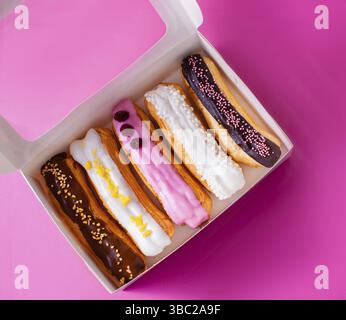 Ein Set köstlicher Eclairs mit verschiedenen Füllungen, die in einer Geschenkbox auf pinkfarbenem Hintergrund liegen Stockfoto