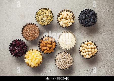Set aus Schüsseln mit gesunden getrockneten Früchten und leckeren Nüssen auf grauem Hintergrund, flach liegend. Cashew, Walnuss, Nüsse, Cranberry, Rosinen, Leinen, Sesam, kandierte Stockfoto
