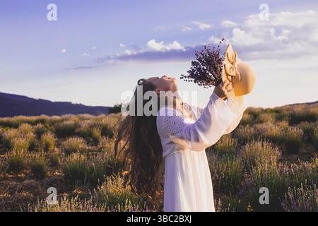 Porträt einer schönen blonden Frau, die zwischen den Plantagen von Lavendel steht. Mädchen in einem weißen Sundress gekleidet und hält sbunch Lavendel Stockfoto