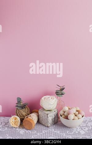 Vertikales Stillleben auf pinkfarbenem Hintergrund. Schüssel mit Filzballen, weißer Würfel mit Rose oben, Geflechtband, gestrickte Tischdecke. Speicherplatz kopieren Stockfoto