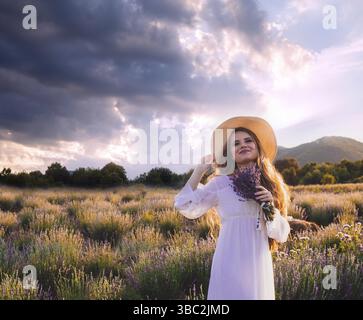 Porträt einer schönen blonden Frau, die zwischen den Plantagen von Lavendel steht. Mädchen in einem weißen Sundress gekleidet und hält sbunch Lavendel Stockfoto