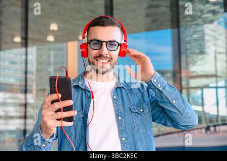 Lächelnder Mann, der Musik mit roten Kopfhörern und Smartphone im Freien hört Stockfoto