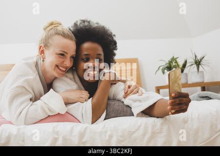 Zwei junge Frauen liegen auf dem Bett und machen Selfies. Die Frauen in Bademänteln ruhen sich nach den Spa-Behandlungen aus Stockfoto