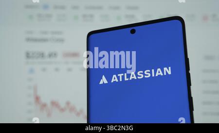 Person, die ein Mobiltelefon mit dem Logo des australischen Softwareunternehmens Atlassian Corporation auf dem Bildschirm vor der Webseite hält. Schwerpunkt auf dem Display des Telefons Stockfoto