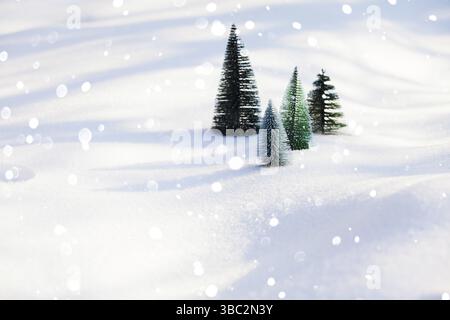 Mehrere künstliche kleine grüne synthetische Tannen stehend auf einem glitzernden frostigen Schnee. Schneeflocken fallen vor der Bäume. Hintergrundbild Stockfoto