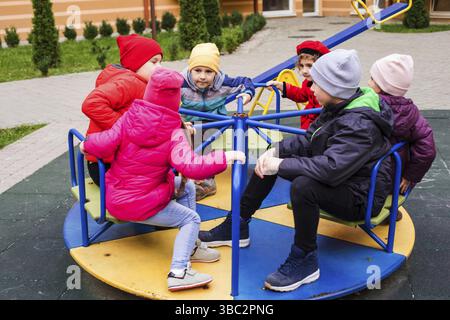 Kinder spielen auf dem Spielplatz im Freien im Frühling. Mädchen sitzt auf einem Karussell. Schöne Zeit auf dem Spielplatz. Frohe Kindheit Stockfoto