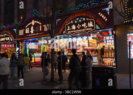 Shanghai, China - 1. April 2025: Touristen und Einheimische shoppen und Fotos in der bunten beleuchteten Snackstraße an der Nanjing Road in Shanghai Stockfoto