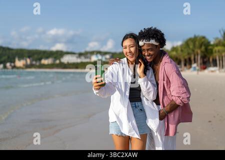 Vielfältige Paare verbunden, mit Technologie und sozialen Medien, während Sie Momente am Strand genießen Stockfoto