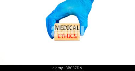 Medizinethik-Symbol. Konzeptworte medizinische Ethik auf schönen Holzblöcken. Arzthand in blauem Handschuh. Schöner weißer Hintergrund. Medizinische Heilung Stockfoto