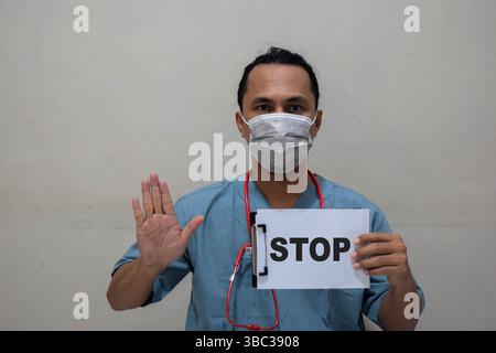 Junger Doktor Mann zeigt Stop Geste und hält Papier mit Text Stop for Fighting Virus Stockfoto