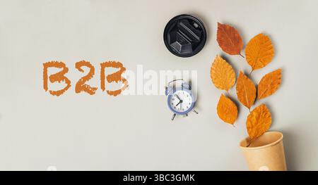 Die Uhr steht auf einem Tisch mit einer Laubpflanze. Das Wort B2B wird in orangefarbenen Buchstaben geschrieben Stockfoto