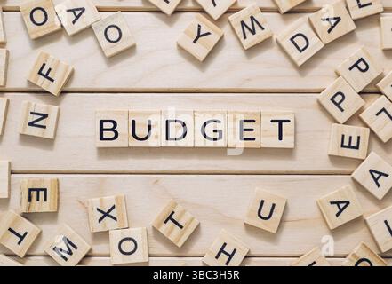 Holzbrett mit einem Haufen Buchstaben und dem Wort Budget in der Mitte. Die Buchstaben sind überall auf dem Brett verstreut Stockfoto