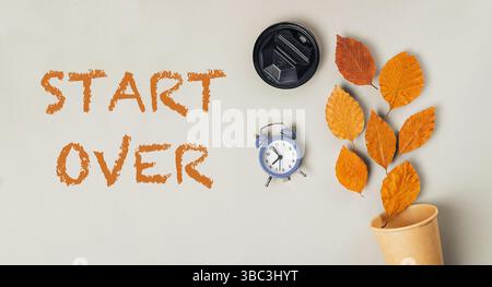 Die Uhr steht auf einem Tisch mit Blättern, und die Worte beginnen zu früh an die Wand geschrieben. Die Uhr ist blau und weiß Stockfoto