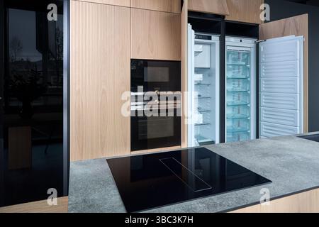 Moderne Einbauküche mit minimalistischem, flachem Design mit gestreiften Holzschränken, eingebautem Backofen, Mikrowelle und leerem Kühlschrank mit geöffnetem DO Stockfoto