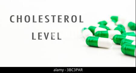 Die grüne und weiße Pille ist auf weißem Hintergrund. Die Pille ist als Cholesterinspiegel gekennzeichnet. Es gibt viele Pillen im Hintergrund Stockfoto