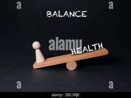 Holzwaage mit einer Person auf der einen Seite und der Wortwahl auf der anderen. Das Wort Gesundheit steht auf der Skala Stockfoto