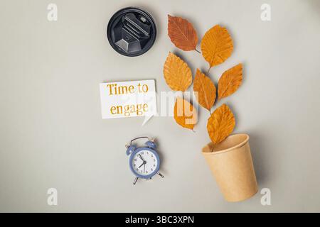 Die Uhr steht auf einem Tisch neben einem Becher und einer grünen Pflanze. Zeit für engagiertes, Schulkonzept Stockfoto