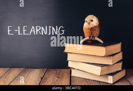 Niedliche kleine Eule steht auf einem Stapel Bücher, die auf einer Holzfläche gestapelt sind. Back-to-School-Konzept Stockfoto