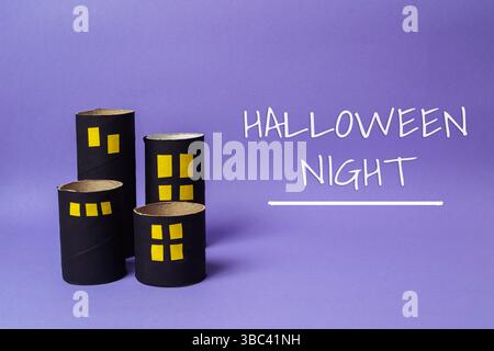 Papphaus mit einem Schild, auf dem die Halloween-Nacht steht. Das Schild ist auf violettem Hintergrund. Die Häuser bestehen aus Pappe und sind in einer Reihe angeordnet Stockfoto