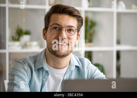 Porträt eines selbstbewussten jungen Mannes mit Brille, der die Kamera anlächelt, während er von zu Hause aus arbeitet Stockfoto