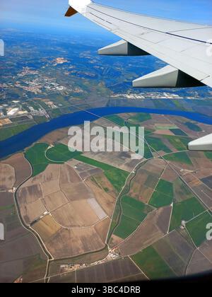 Panoramablick aus der Vogelperspektive auf bewirtschaftete Felder mit Bewässerungskanälen und einem breiten blauen Fluss unter sonnigem Himmel vom Flugzeugfenster aus Stockfoto