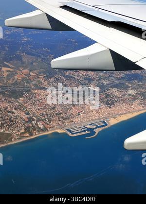 Küstenstädte aus dem Flugzeug, das die Yachthafenboote am Strand und die städtische Entwicklung unter sonnigem Himmel zeigt Stockfoto