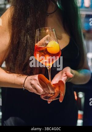 Nahaufnahme einer Frau mit einem eleganten Orangencocktail und einer runden Eiskugel, serviert in einem Weinglas an einer Bar. Stockfoto