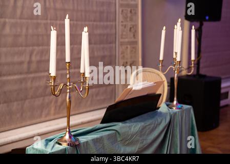 Zwei goldene Kerzenleuchter mit weißen Kerzen schaffen ein warmes und klassisches Ambiente für eine formelle oder romantische Zusammenkunft. Stockfoto