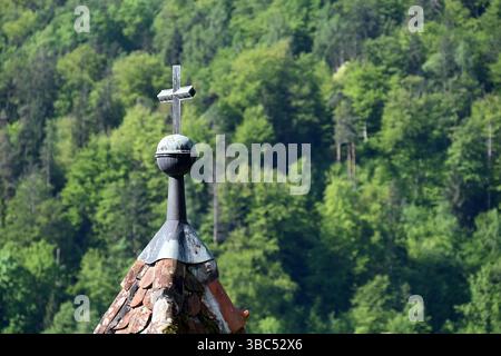 Kleines Kreuz auf altem Dach gegen grünen Wald im Frühling auf der Insel Bled, Slowenien Stockfoto
