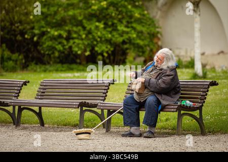 Ein älterer Mann mit weißen Haaren spielt im Frühling auf einer Bank im Park ein altes Drehradio Stockfoto