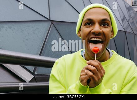 Nahaufnahme eines glücklichen jungen Mannes, der draußen in der Stadt einen Lutscher genießt Stockfoto